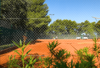 Udsigt til en tennisbane med rødt ler og grønne planter på Camping Lanterna feriested i Istrien, Kroatien.