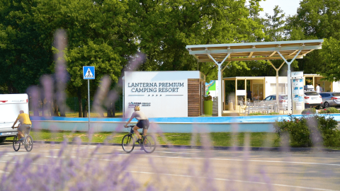 Due ciclisti passano davanti all'ingresso di Lanterna Premium Camping Resort in Istria, Croazia, tra gli alberi.