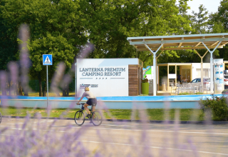 Due ciclisti passano davanti all'ingresso di Lanterna Premium Camping Resort in Istria, Croazia, tra gli alberi.