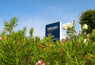 Skiltet til Lanterna Premium Camping Resort titter frem bag grønne buske og blomster under en klar himmel i Istrien.