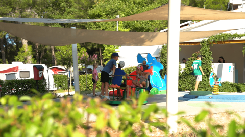 Bambini giocano sotto teli ombreggianti al Camping Lanterna in Istria, Croazia, circondati da roulotte e verde.