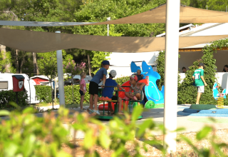 Børn leger under solsejl på Camping Lanterna i Istrien, Kroatien, omgivet af campingvogne og grønne områder.