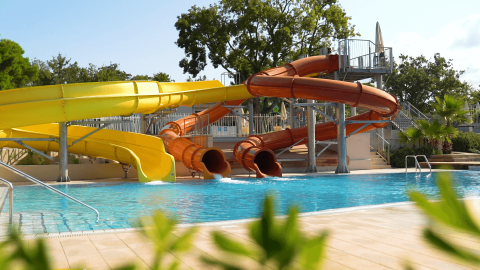 Toboganes acuáticos en la piscina de Camping Lanterna, un parque vacacional en Istria, Croacia, entre árboles.