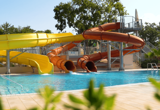 Vandrutsjebaner ved en swimmingpool i Camping Lanterna, en feriepark i Istrien, Kroatien, omgivet af træer.