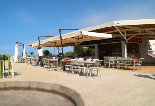 Area esterna del bar al Camping Lanterna in Istria, Croazia, con tavoli, sedie e grandi ombrelloni al sole.