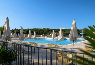Area piscina all'aperto con lettini e ombrelloni al Camping Lanterna, Istria, Croazia, sotto cielo sereno.