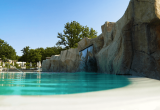 Piscina al Camping Lanterna in Istria, Croazia, con parete rocciosa, cascata e lettini sotto il cielo azzurro.