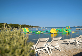 Lettini sulla spiaggia con vista su un parco acquatico gonfiabile al Camping Lanterna, Istria, Croazia.