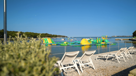 Ligstoelen bij een kiezelstrand met uitzicht op een opblaasbaar waterpark bij Camping Lanterna, Istrië, Kroatië.