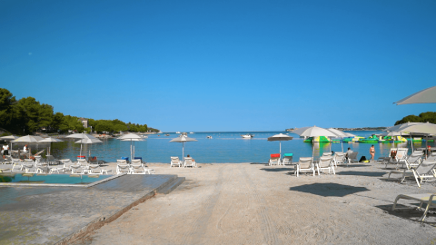Playa soleada en Camping Lanterna, Istria, Croacia, con tumbonas, sombrillas y mar azul tranquilo.
