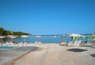 Playa soleada en Camping Lanterna, Istria, Croacia, con tumbonas, sombrillas y mar azul tranquilo.