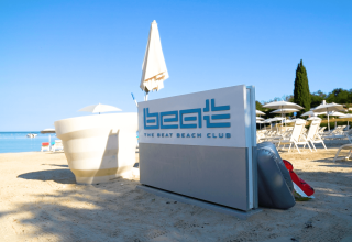 Cartel de club de playa y tumbonas en la arena de Camping Lanterna, Istria, Croacia, bajo un cielo azul despejado.