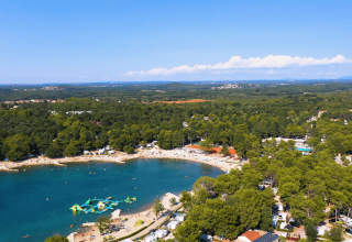 Luftfoto af Camping Valkanela i Istrien, Kroatien, med strand, hav og ferieboliger omgivet af grønne træer.