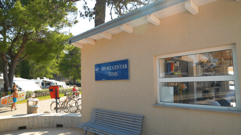 Edificio Sport Center Tenis con banco afuera, rodeado de árboles en Camping Valkanela, Istria, Croacia