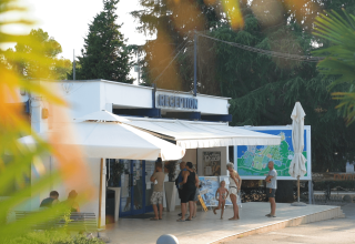 Folk står foran receptionen ved Camping Valkanela feriepark i Istrien, Kroatien, omgivet af grønne træer.