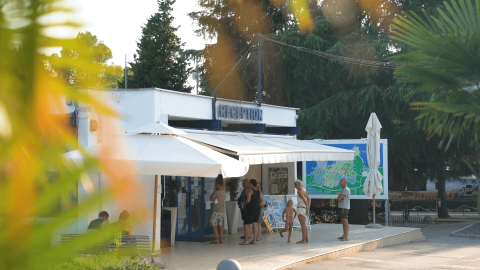 Persone davanti alla reception del Camping Valkanela in Istria, Croazia, circondate dal verde degli alberi.