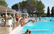 Feriepark poolområde med folk, børn der springer i vandet, parasoller og liggestole ved Camping Valkanela.