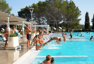 Feriepark poolområde med folk, børn der springer i vandet, parasoller og liggestole ved Camping Valkanela.