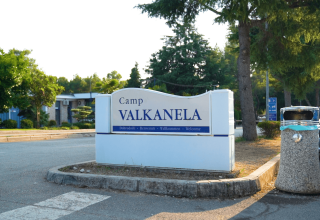 Indgangsskilt til Camp Valkanela, en ferielejr i Istrien, Kroatien, omgivet af træer og parkerede biler.
