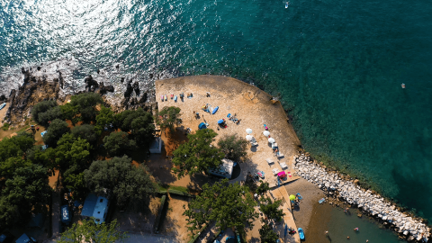 Vista aerea del Camping Valkanela in Istria, Croazia, con spiaggia di ciottoli, mare blu e vegetazione.