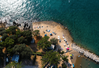Luftfoto af Camping Valkanela i Istrien, Kroatien, med stenstrand, klart blåt hav og grønne træer.