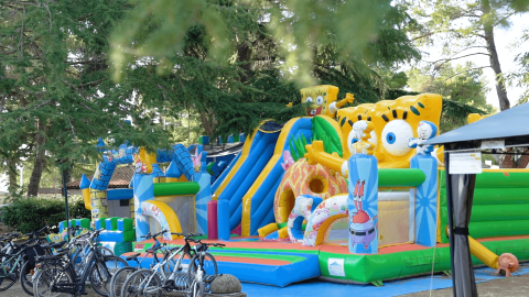 Parque infantil hinchable de Bob Esponja con bicicletas delante, rodeado de árboles en Camping Valkanela, Istria.