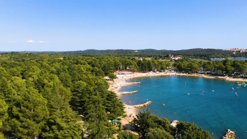 Aerial view of Camping Valkanela holiday park in Istria, Croatia, with beach, bay waters and lush green trees.