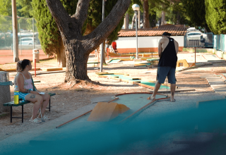 To personer spiller minigolf under træer på Camping Valkanela feriepark i Istrien, Kroatien, på en solrig dag.