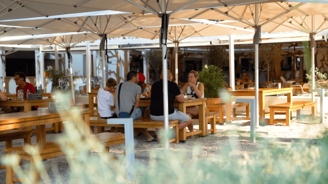 Outdoor dining area with wooden tables and benches under large umbrellas at Camping Valkanela, Istria, Croatia.