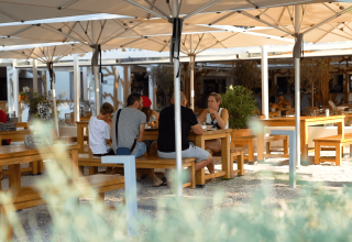 Outdoor dining area with wooden tables and benches under large umbrellas at Camping Valkanela, Istria, Croatia.