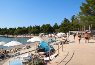 Vista sulla spiaggia dal Camping Valkanela in Istria, Croazia, con ospiti, lettini e ombrelloni bianchi.