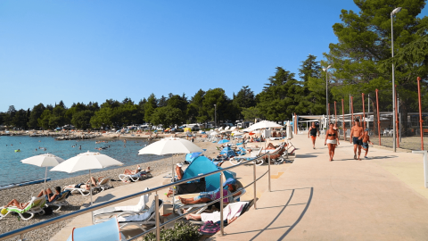 Vue de la plage au Camping Valkanela en Istrie, Croatie, avec vacanciers sur transats et parasols blancs.