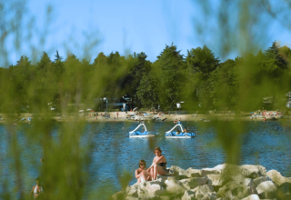 Vista della spiaggia di Camping Valkanela in Istria, Croazia, con persone e pedalò sul lago tra il verde.
