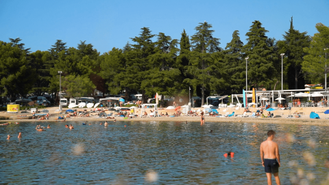 Playa del Camping Valkanela en Istria, Croacia, con bañistas disfrutando junto al agua y árboles al fondo.
