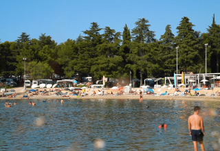 Feriecampingplads ved Camping Valkanela i Istrien, Kroatien, med strand, svømmende gæster og træer bagved.
