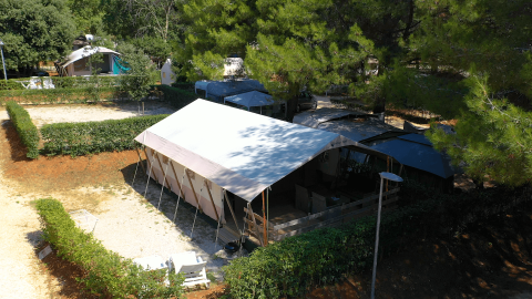 Vista aerea di una grande tenda e area campeggio tra alberi presso il Camping Valkanela in Istria, Croazia.