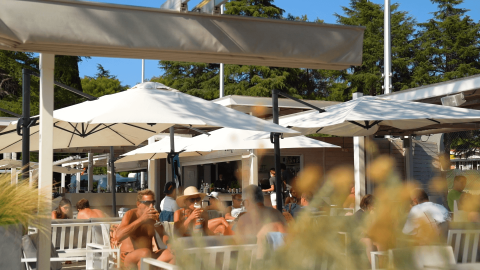 Huéspedes disfrutan bebidas bajo sombrillas en la cafetería al aire libre de Camping Valkanela, Istria, Croacia.