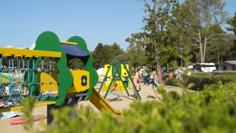 Children's playground at Camping Valkanela holiday park in Istria, Croatia, with trees and camping tents.