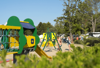 Aire de jeux pour enfants au Camping Valkanela en Istrie, Croatie, entourée d’arbres et de campeurs.