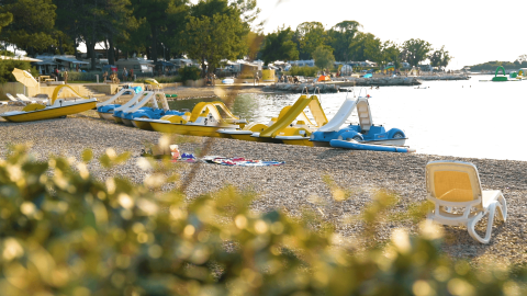 Playa de piedras en Camping Valkanela, Istria, Croacia, con patinetes acuáticos, tumbona y ambiente soleado.