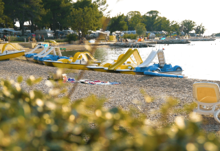 Udsigt over stranden ved Camping Valkanela i Istrien, Kroatien, med vandcykler, liggestol og solrigt vejr.