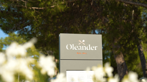 Cartel del restaurante Oleander Real Grill rodeado de árboles en Camping Valkanela, Istria, Croacia.