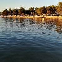 Uitzicht op het water bij een vakantiepark met glamping-accommodaties, omringd door bomen en avondlicht.