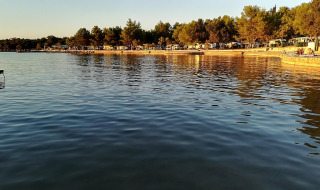 Vue sur l'eau calme d’un parc de vacances proposant du glamping, entouré d’arbres et baigné de lumière dorée.