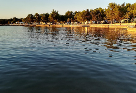 Vista del agua tranquila en un parque vacacional con alojamientos glamping, árboles y luz de atardecer.