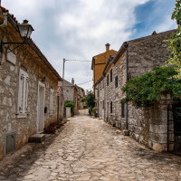 Calle adoquinada en parque vacacional con glamping, rodeada de casas de piedra antigua y vegetación.