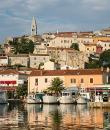 Photo d'une charmante ville côtière avec bateaux, bâtiments colorés, verdure et un clocher en arrière-plan.