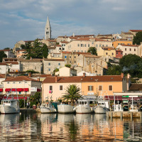 Foto de un pintoresco pueblo costero con barcos, casas coloridas, árboles y una torre de iglesia al fondo.
