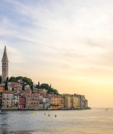 Kuststad met kleurrijke huizen en kerktoren aan zee bij zonsondergang, gezien vanaf een glamping vakantiepark.