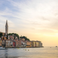 Ville côtière aux maisons colorées et clocher près de la mer, vue au coucher du soleil depuis un glamping.